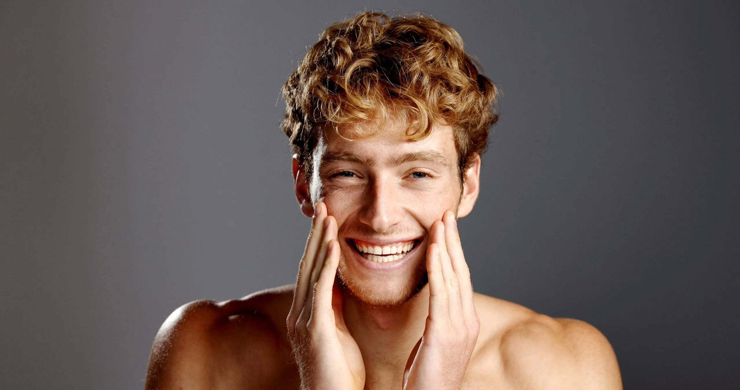Man with curly hair smiling while touching his face
