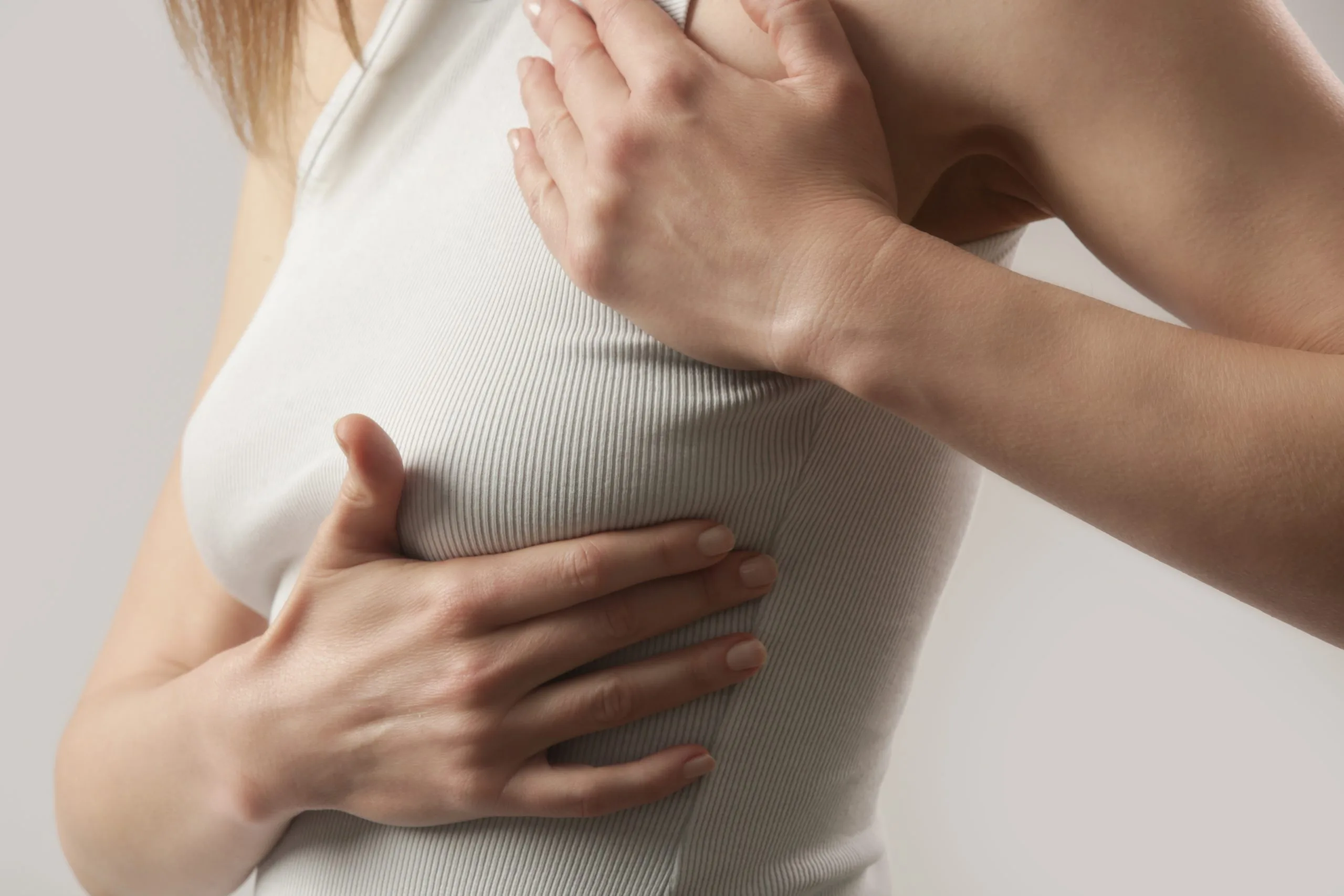 Woman palpating her chest area over white fitted top