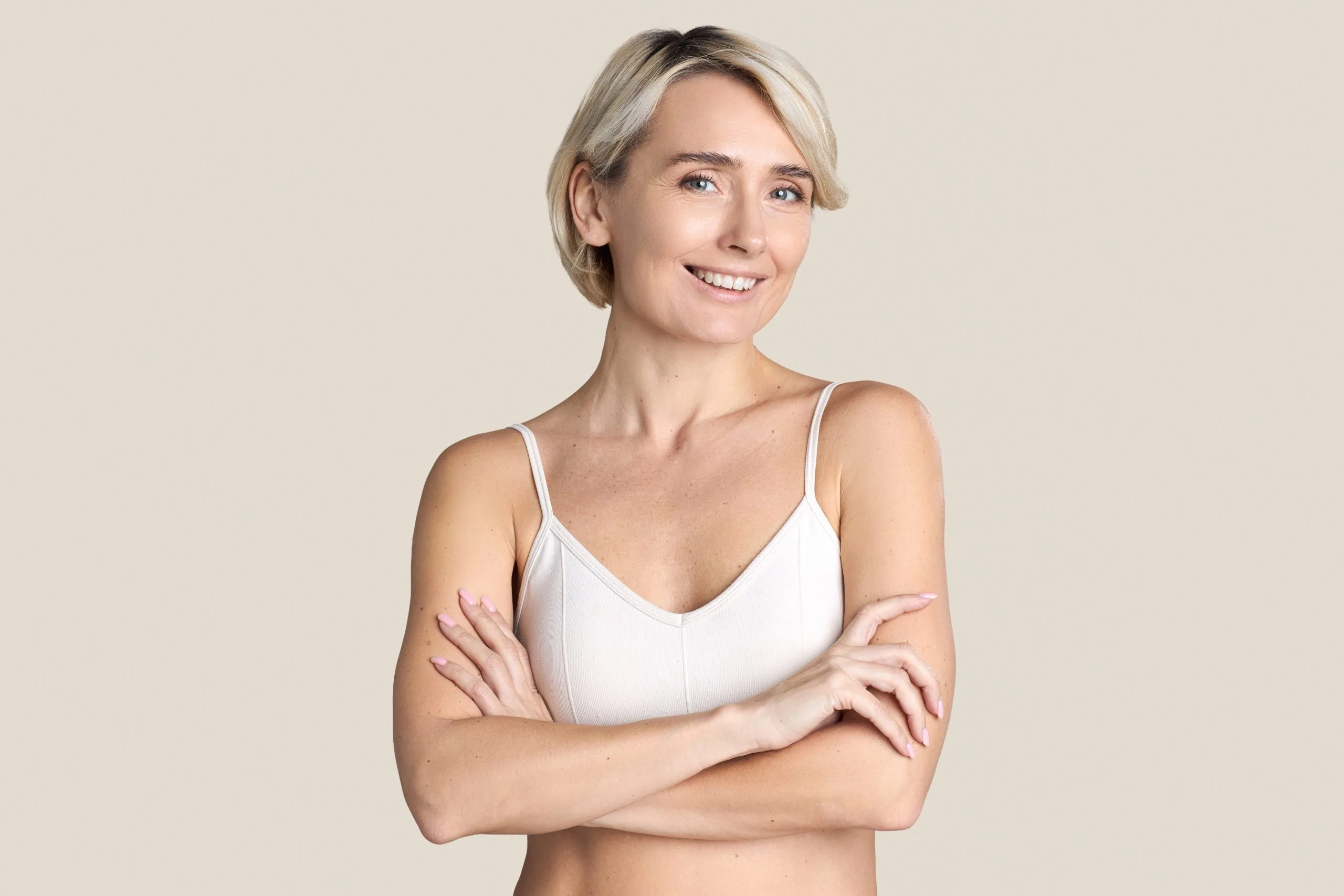 Mature woman with short blonde hair, arms crossed, wearing white camisole