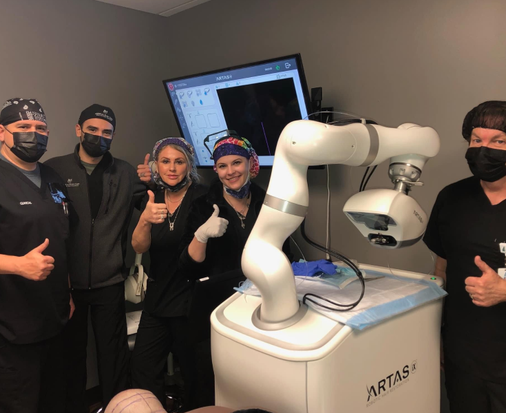 Five staff members in black attire giving thumbs up next to ARTAS robotic hair restoration device