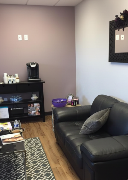 Elysian Plastic Surgery consultation room with black leather sofa, shelving, and treatment equipment