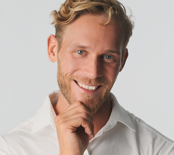 Man in white shirt smiling at camera with hand near chin