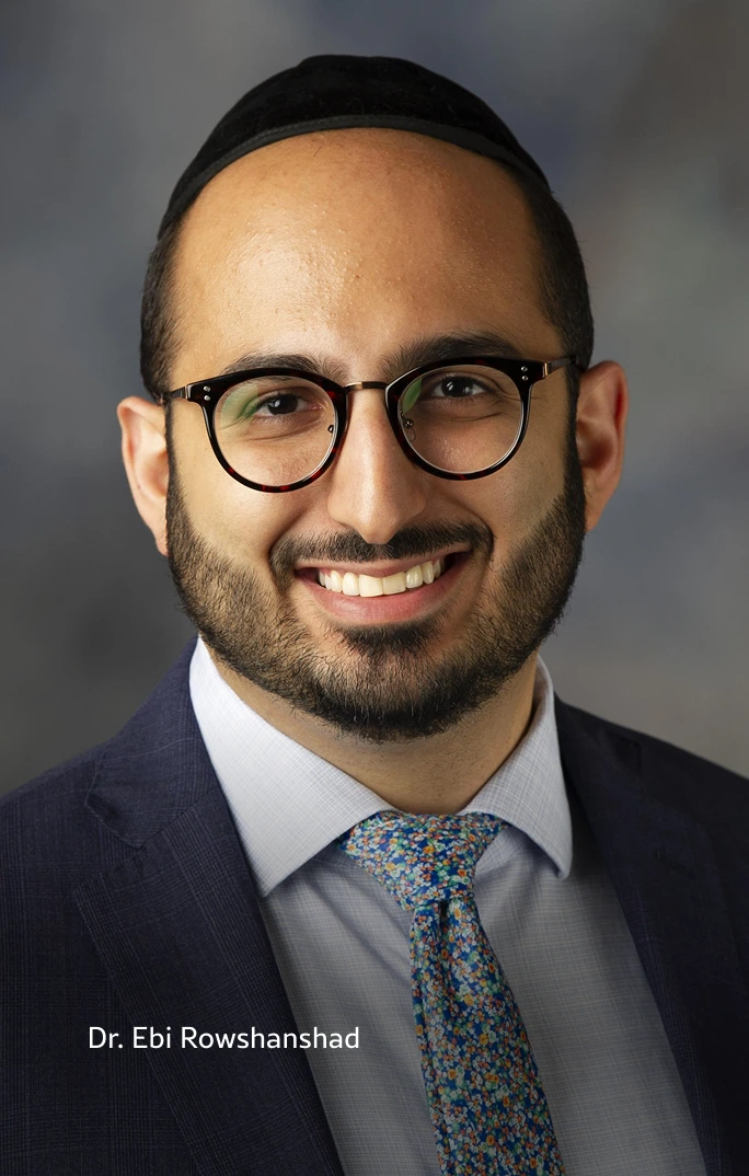 Dr. Ebi Rowshanshad, male physician wearing glasses, dark blazer, and patterned tie, smiling at camera
