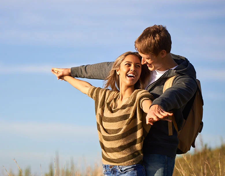 Couple standing in a field with woman extending her arm and smiling at man behind her