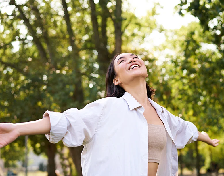 Woman with arms outstretched smiling in sunlit forest setting