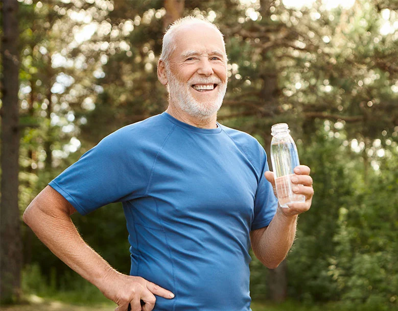 Older man in blue shirt holding water bottle outdoors, smiling