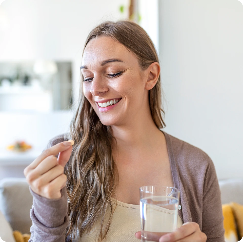 Woman smiling while holding a glass of water and taking a vitamin