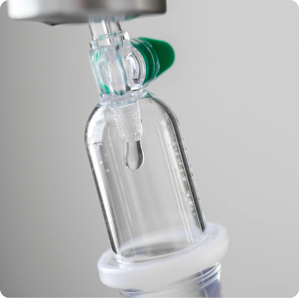 Clear glass dropper bottle with green cap dispensing serum onto white base
