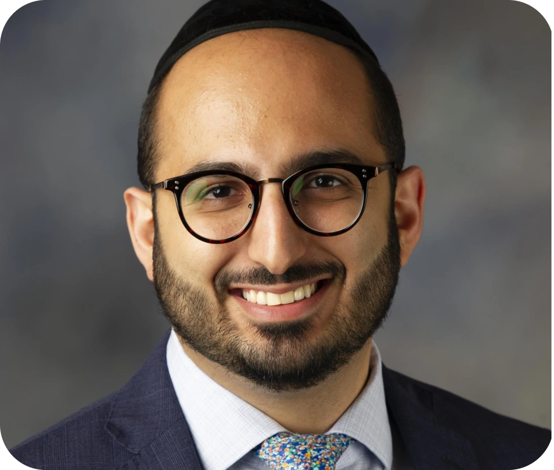 Male healthcare professional wearing glasses and navy blazer, smiling at camera