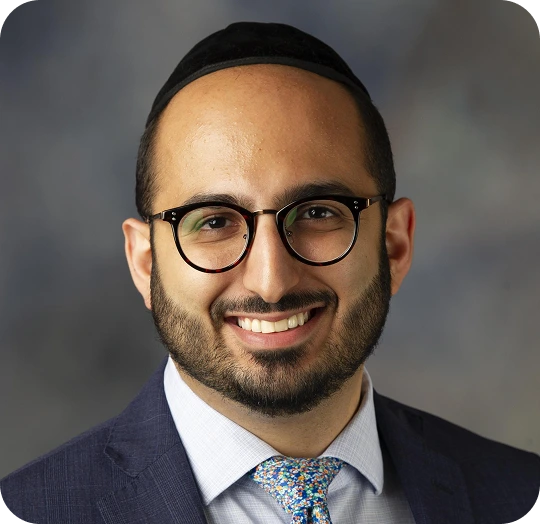 Man wearing glasses, navy suit, and blue patterned tie in professional headshot