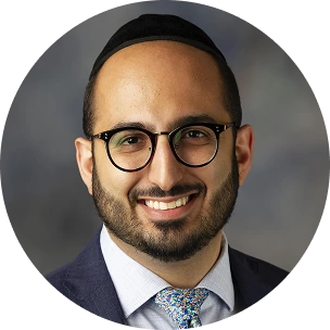 Male healthcare professional wearing glasses and navy blazer, smiling at camera