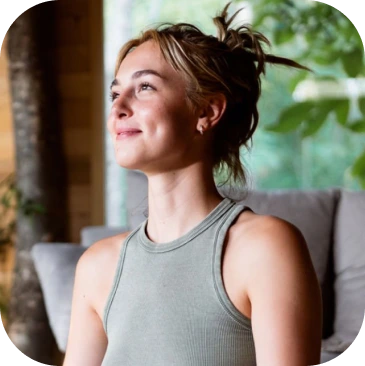 Woman in athletic tank top sitting on a couch near a window with plants