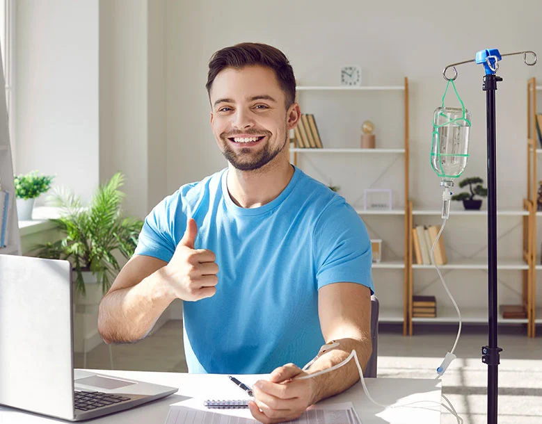 Man receiving IV therapy at home, giving thumbs up while connected to intravenous drip