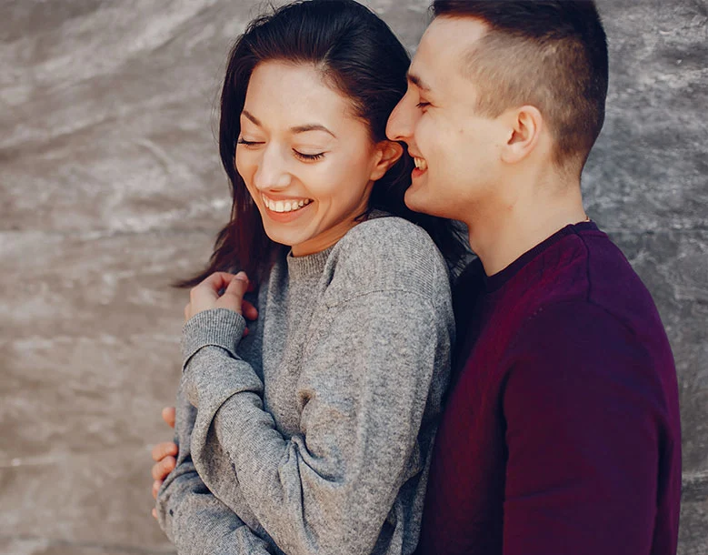 Couple embracing and smiling together against textured gray wall