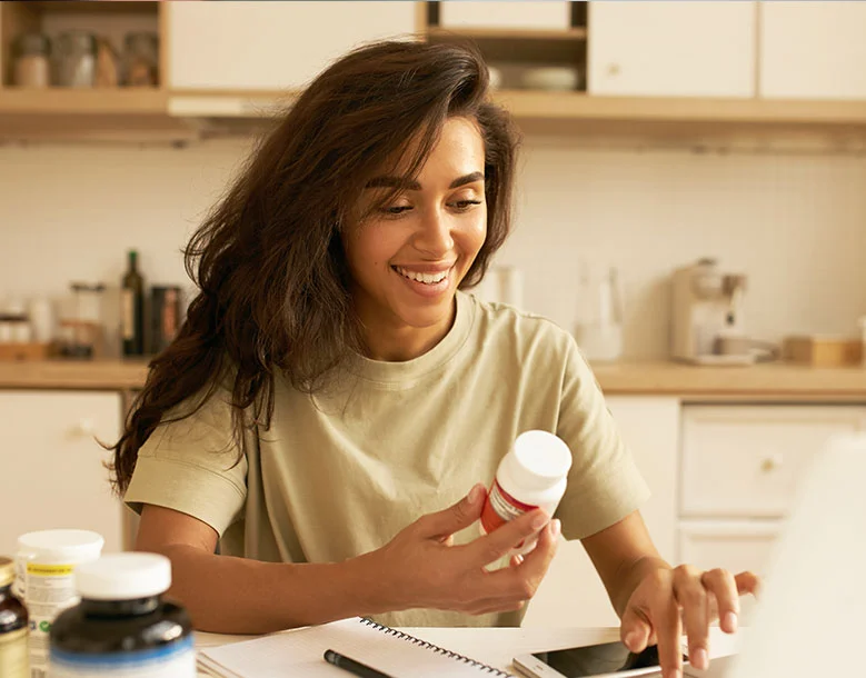 Woman in kitchen reviewing a medication bottle with other pills and containers on table