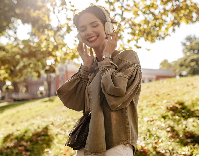 Woman wearing headphones outdoors in park, smiling with eyes closed