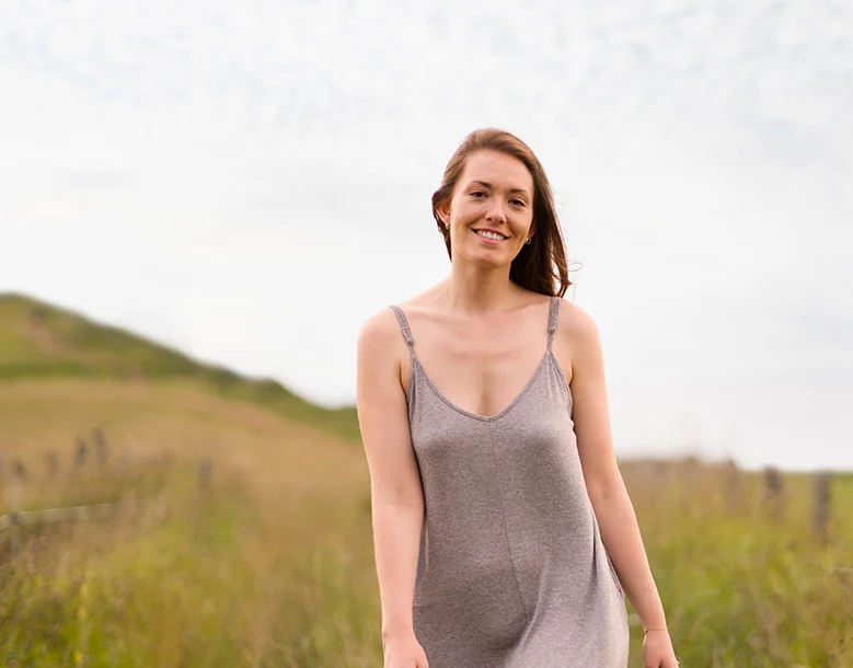 Woman smiling in an open field wearing a gray tank top