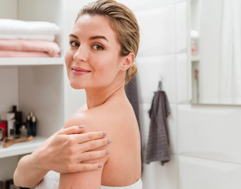 Woman in a bathroom touching her shoulder, looking toward mirror