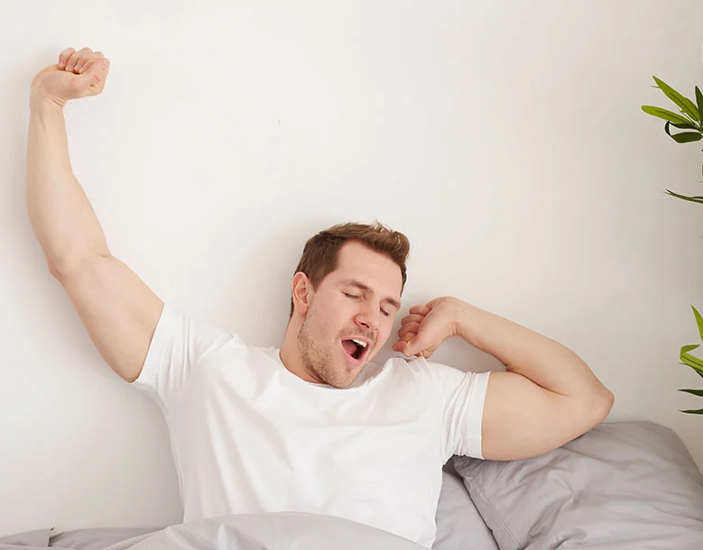 Man stretching in bed with arms raised, yawning while waking up