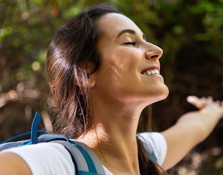 Woman in profile smiling outdoors with arms extended