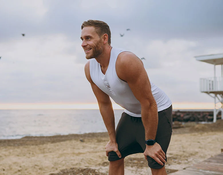 Man stretching before exercise on beach with ocean and lifeguard tower behind