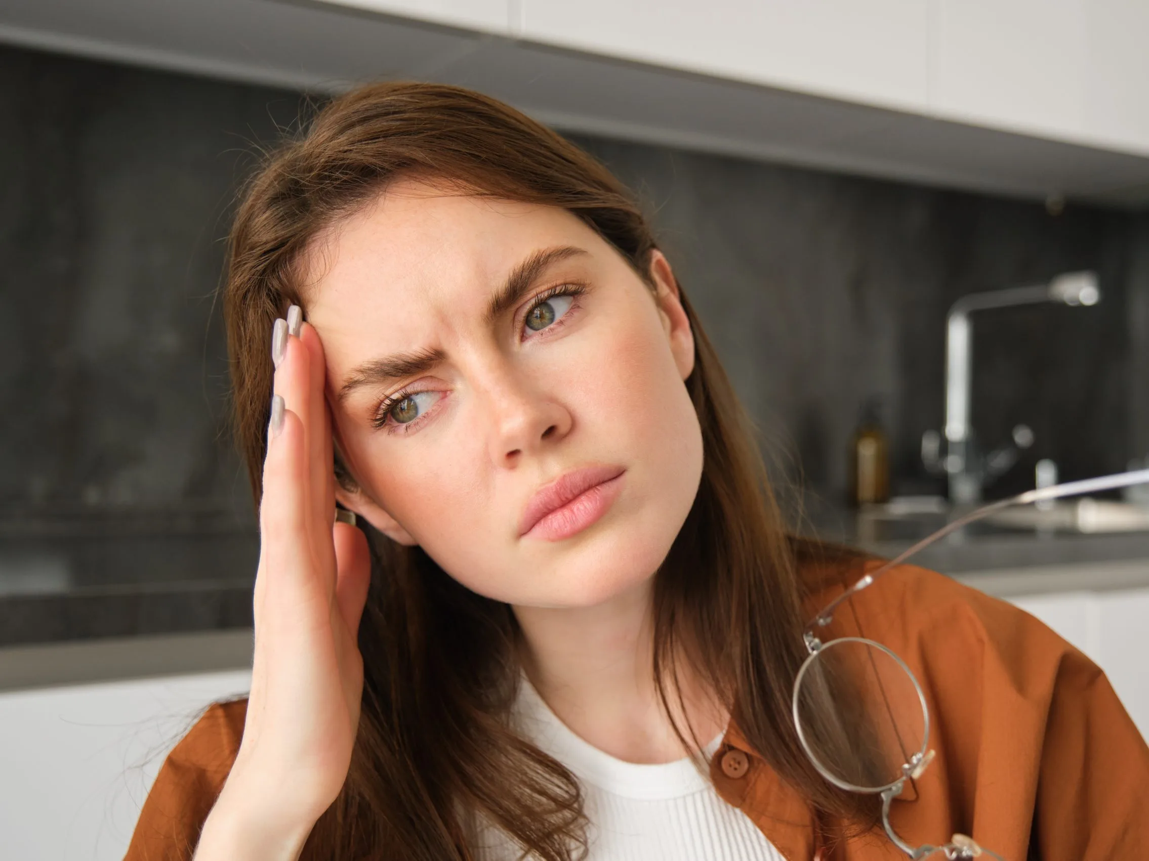 Woman touching her temple with a pained expression, depicting migraine discomfort