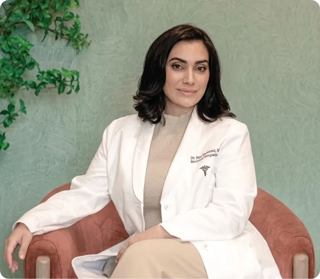 Dermatologist in white coat sitting on rust-colored chair against green-textured wall with plant