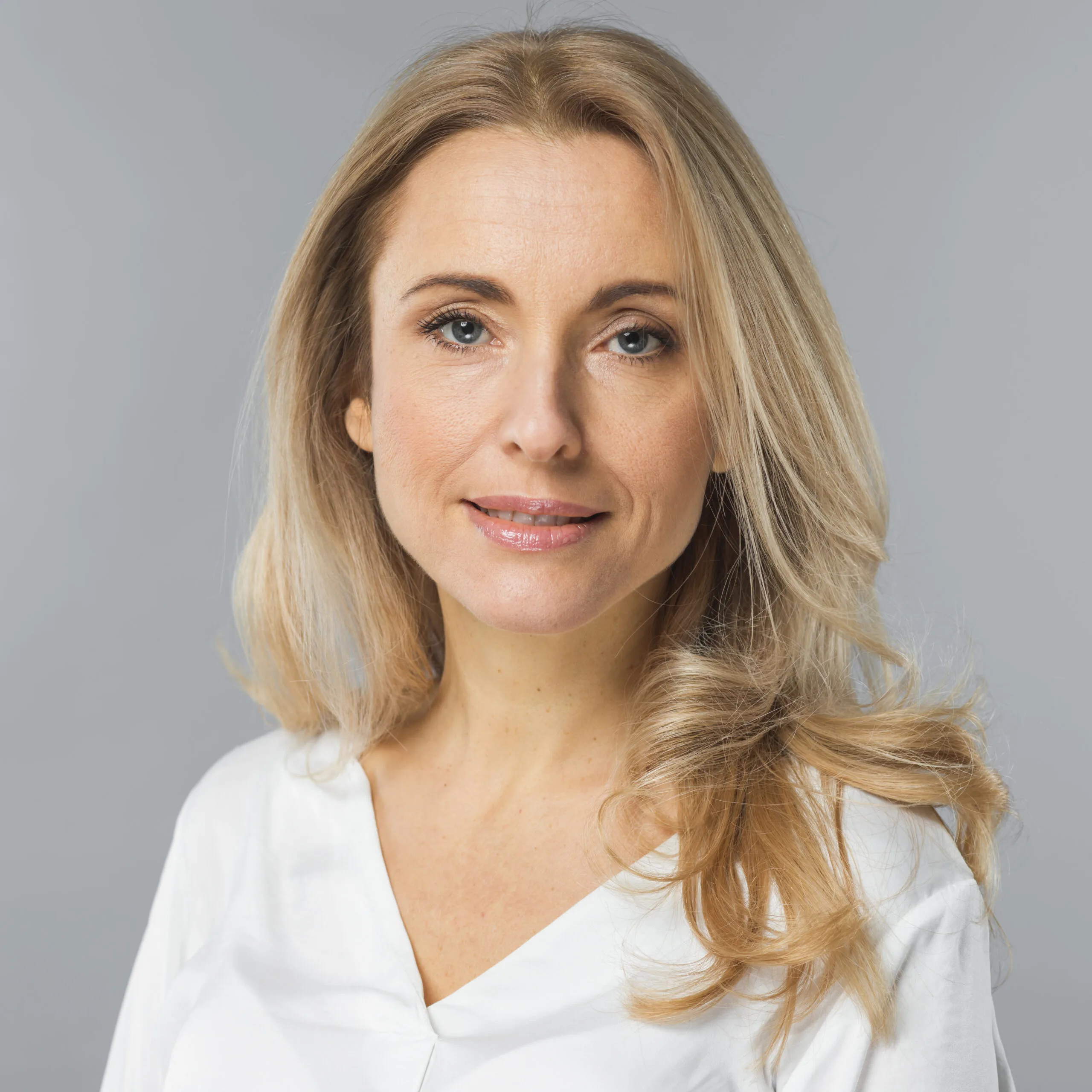 Woman with blonde hair wearing white v-neck top against gray background