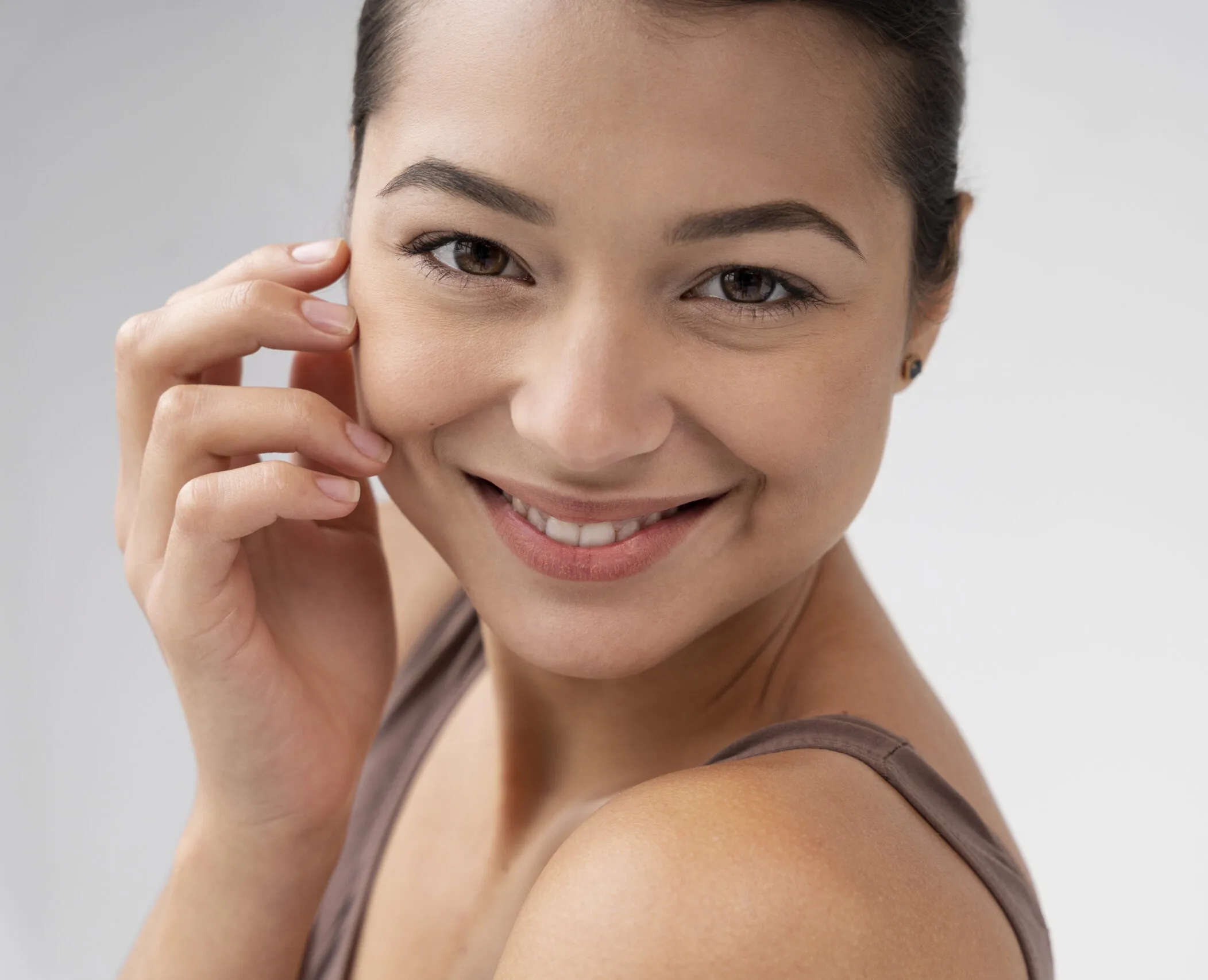 Woman touching her cheek and smiling at the camera against a neutral background