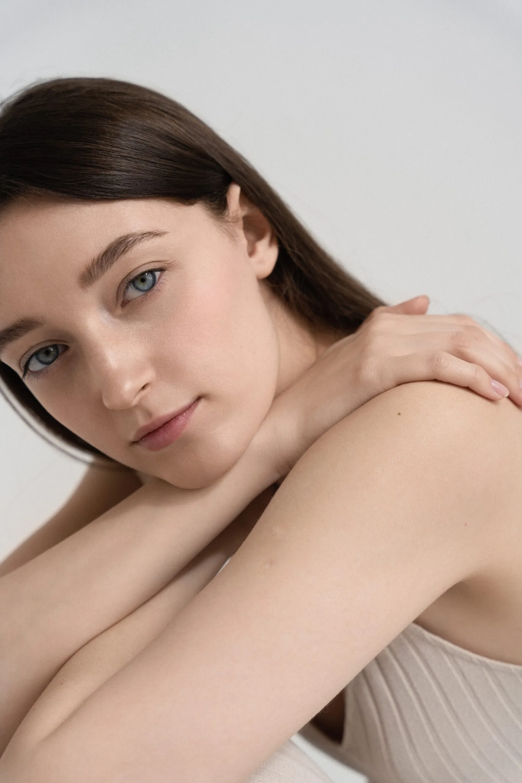 Woman with smooth, glowing skin touching her shoulder against a neutral background
