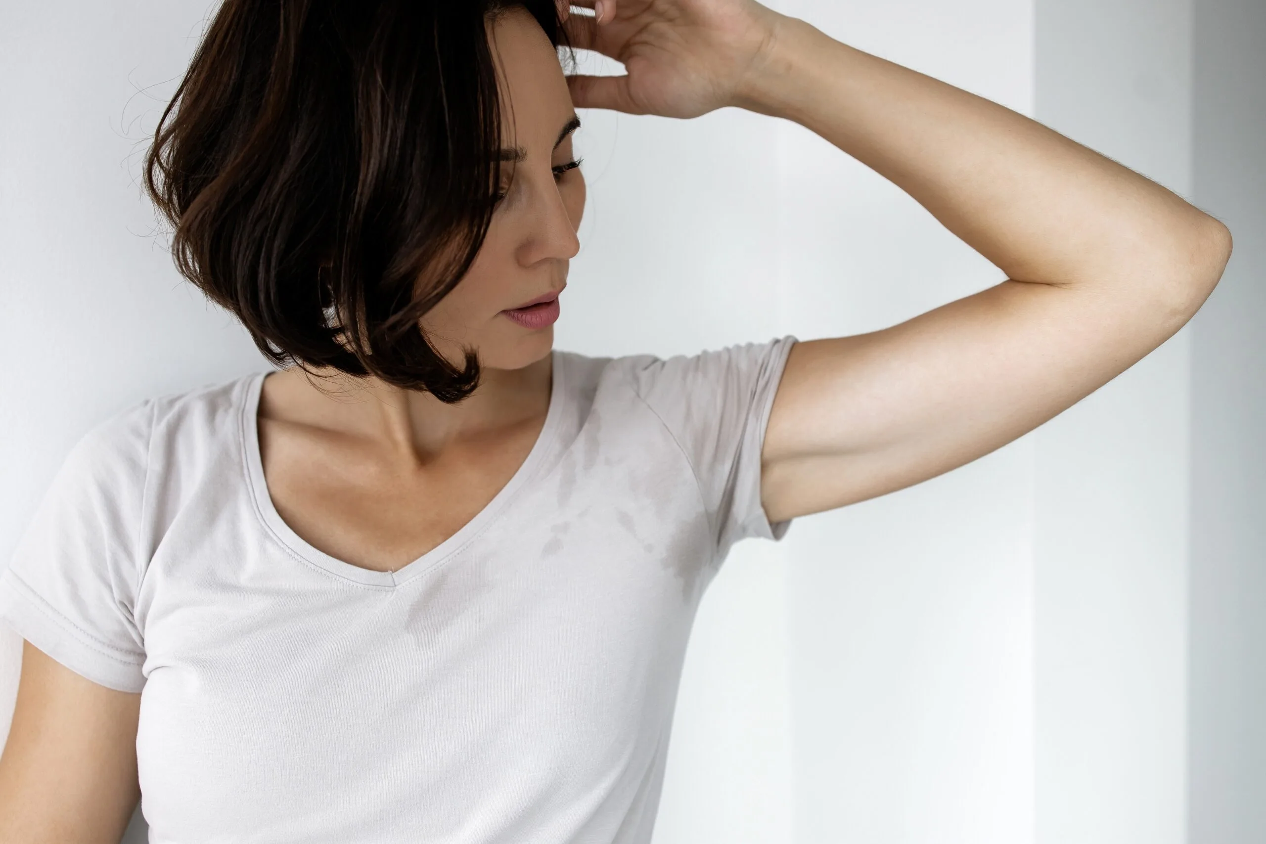 Woman in white t-shirt with arm raised showing underarm area, illustrating excessive sweating concern