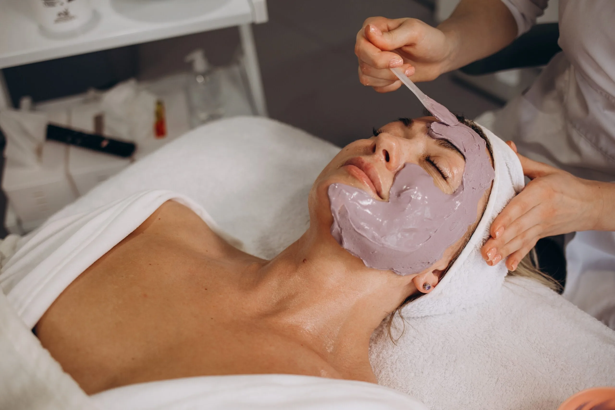 Esthetician applying a purple facial mask to a relaxed patient during a facial treatment at Everoak Dermatology & Aesthetics Center