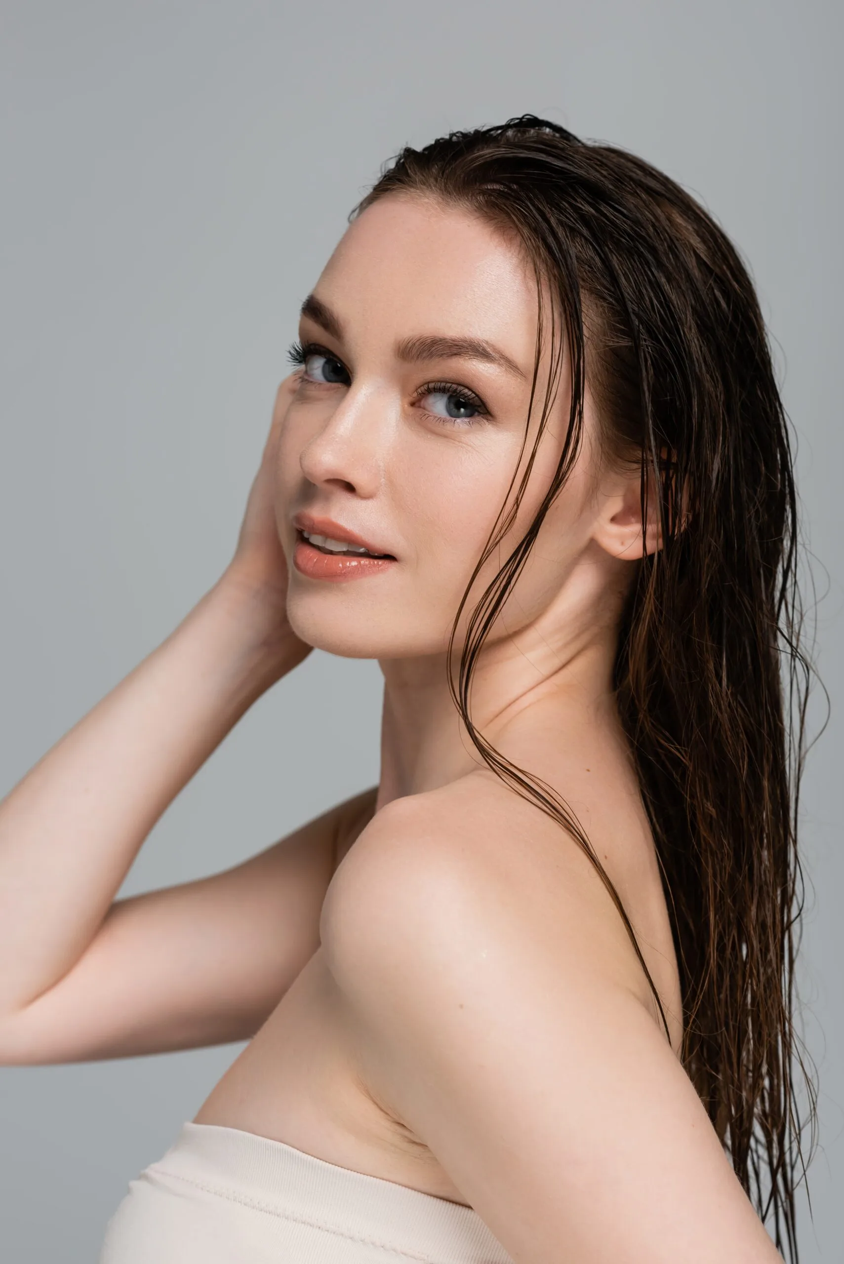 Woman with clear, glowing skin touching her face against a neutral background