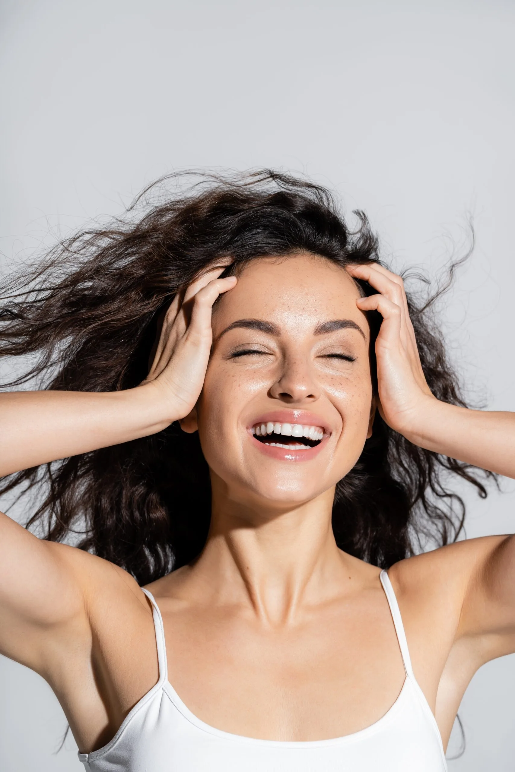Woman smiling with hands on her head, displaying glowing, clear skin
