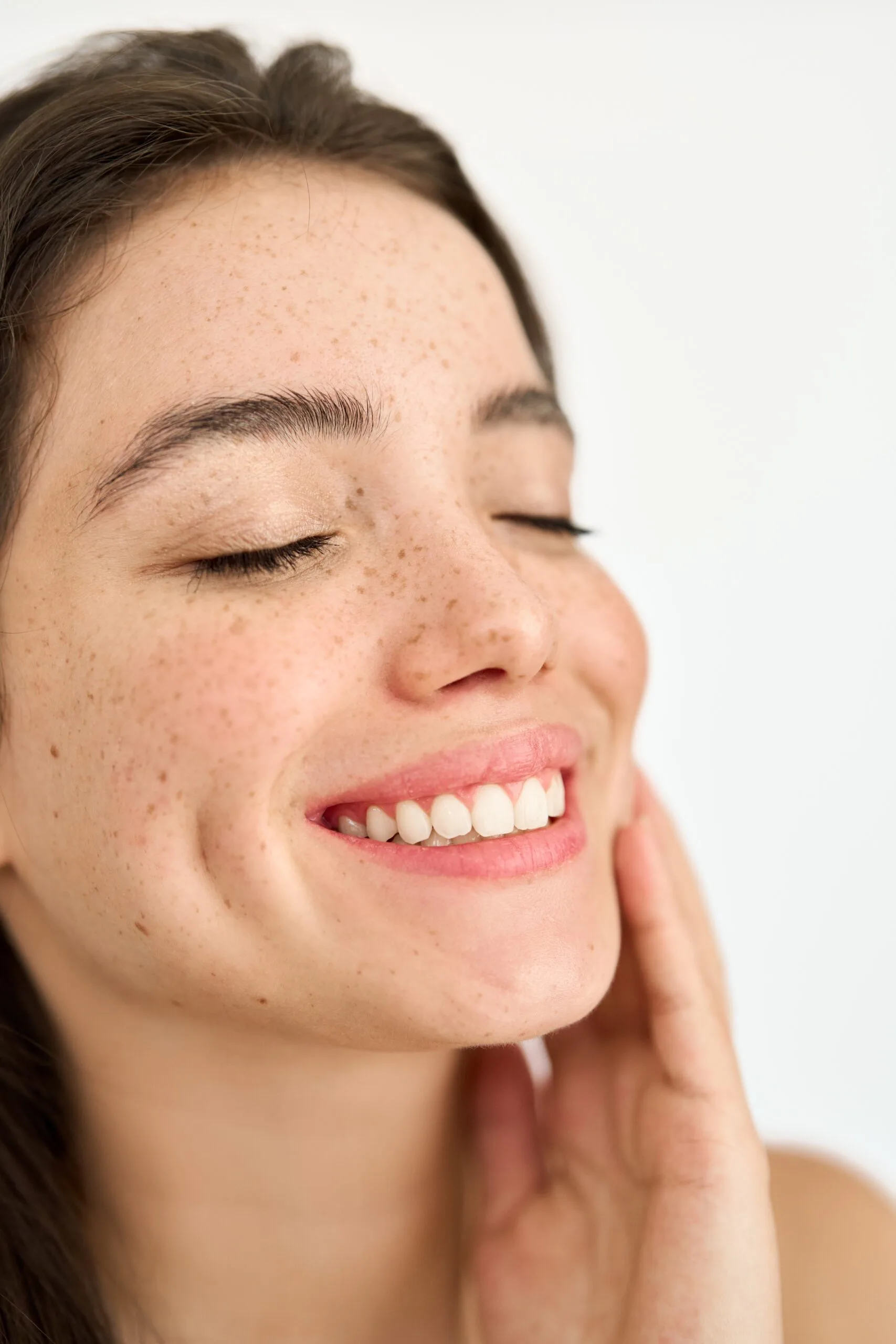 Woman with clear, glowing skin smiling with hand touching her face