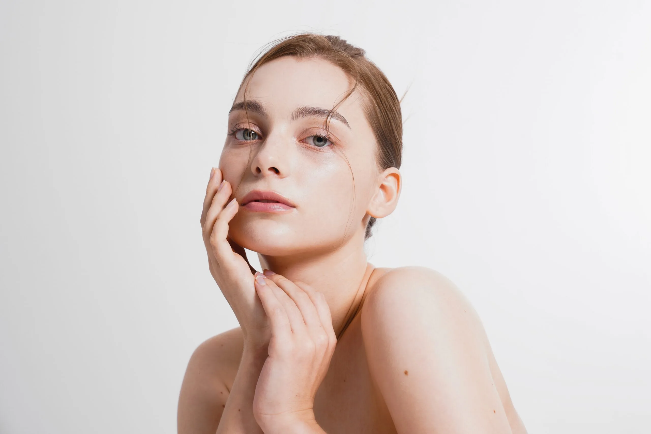 Woman with clear, glowing skin touching her face against a neutral background