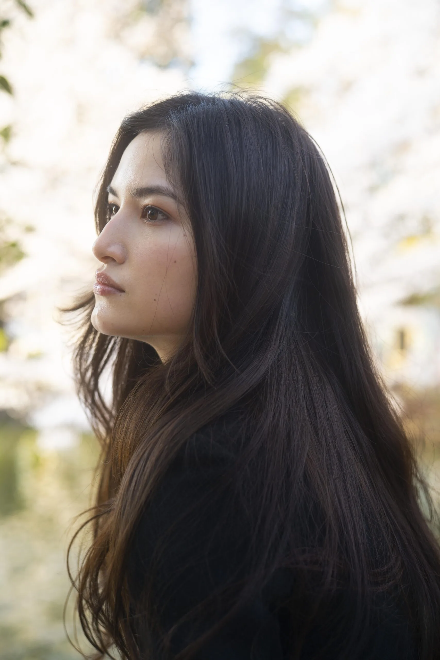 Woman with long, full dark hair shown in profile outdoors