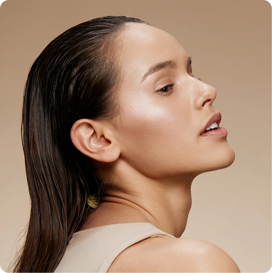 Woman in profile with clear skin and long dark hair against neutral background