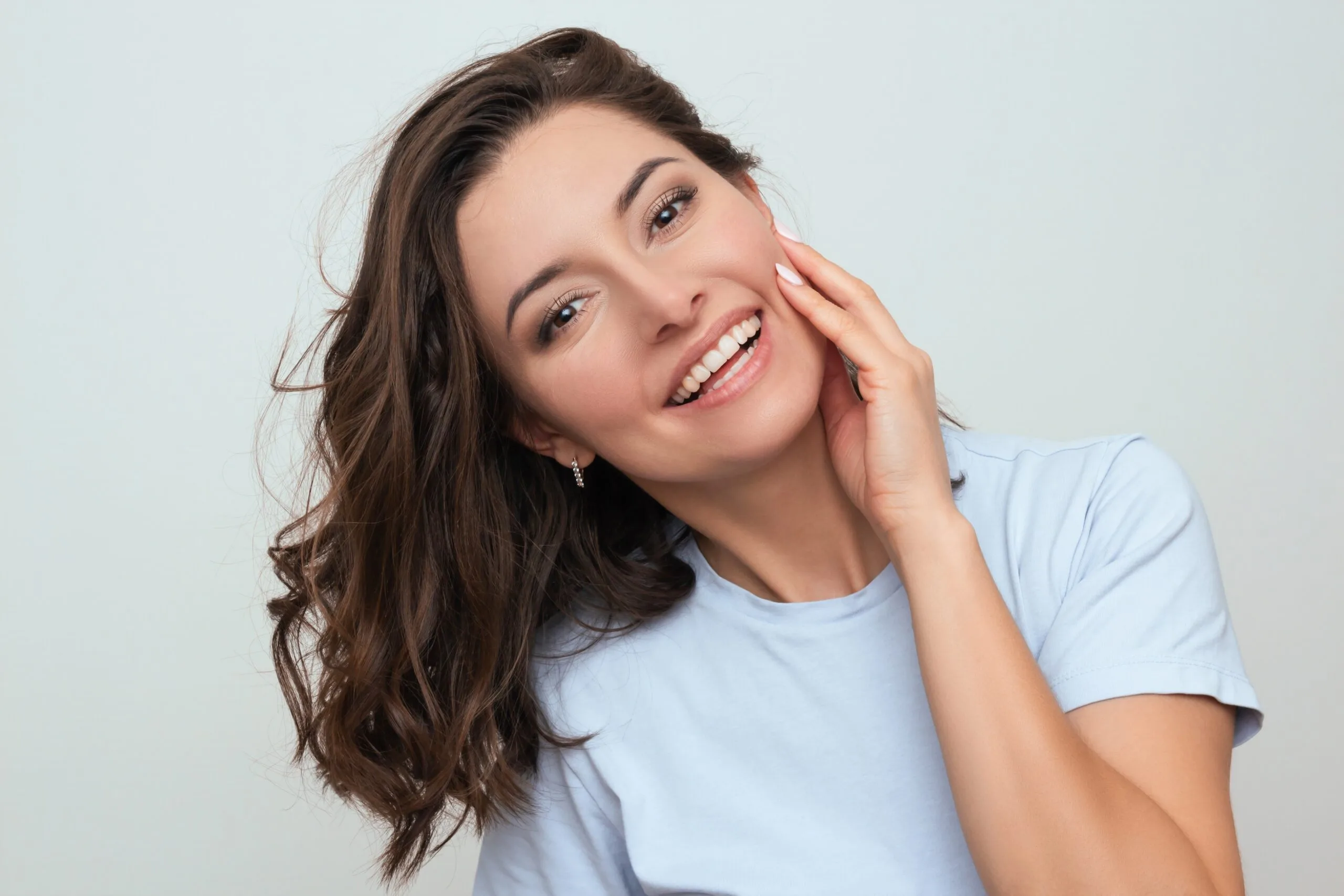 Woman touching her cheek and smiling, demonstrating facial volume and skin results
