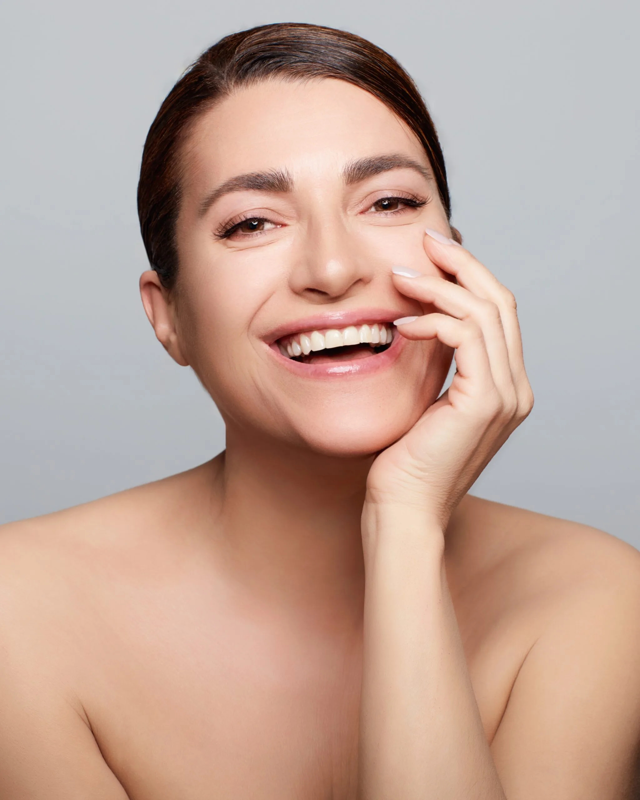 Woman smiling with hand to face, showing smooth skin and lifted cheekbones