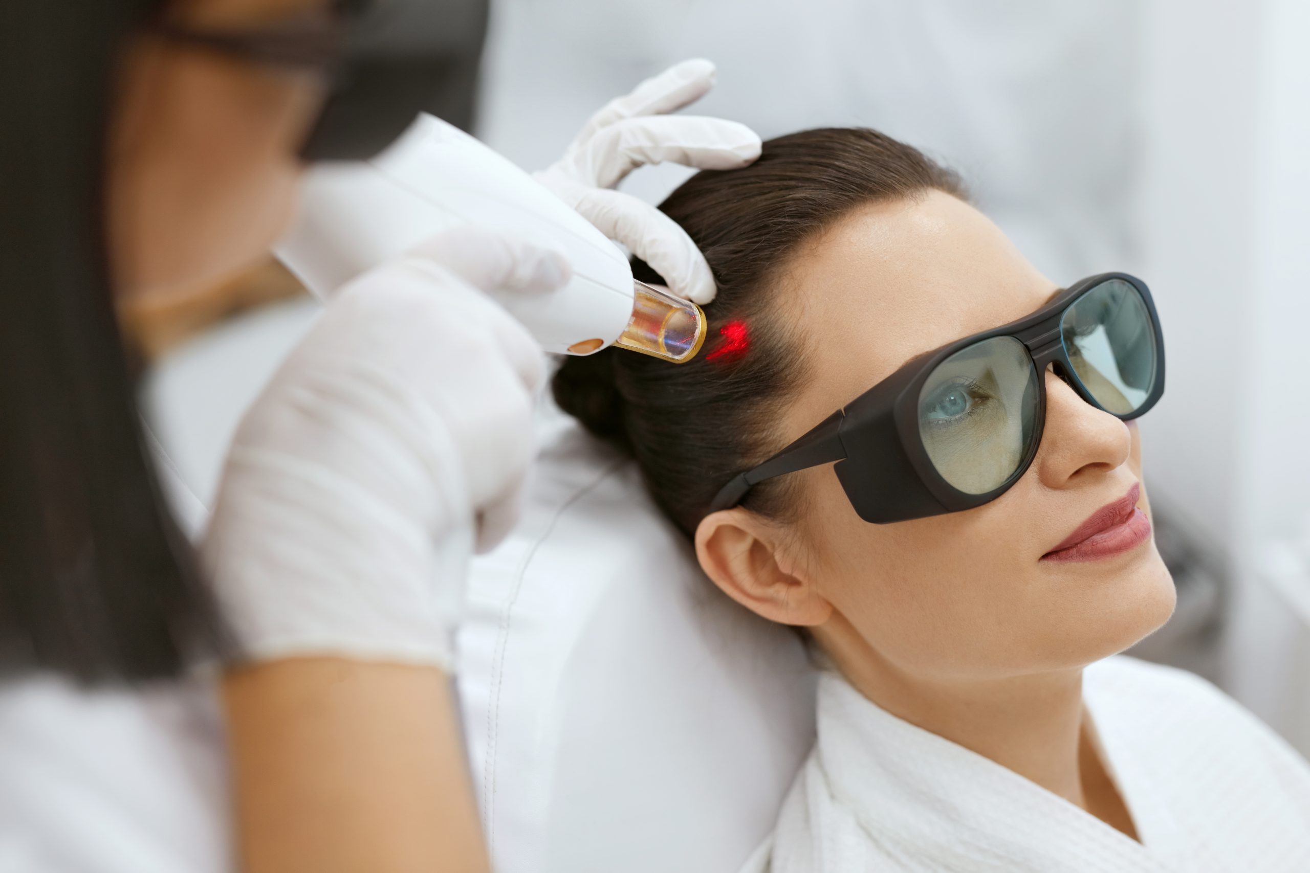 Gloved hands positioning protective eyewear on patient's face during laser treatment