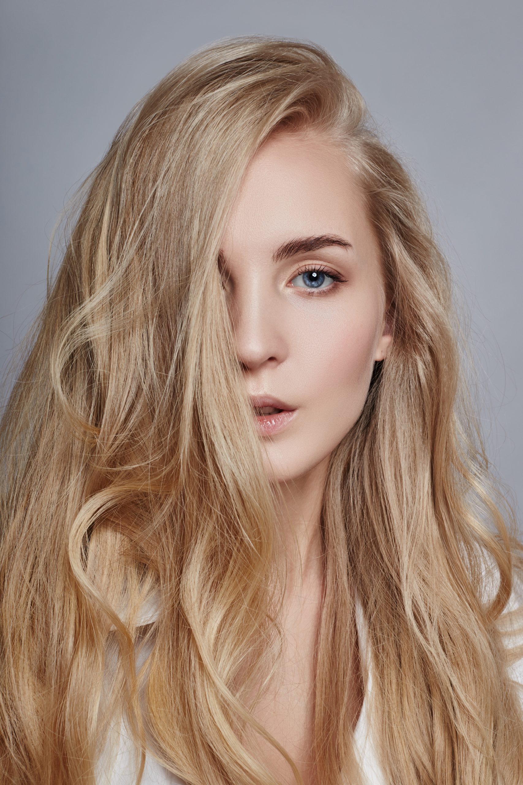 Woman with long blonde wavy hair in profile against gray background