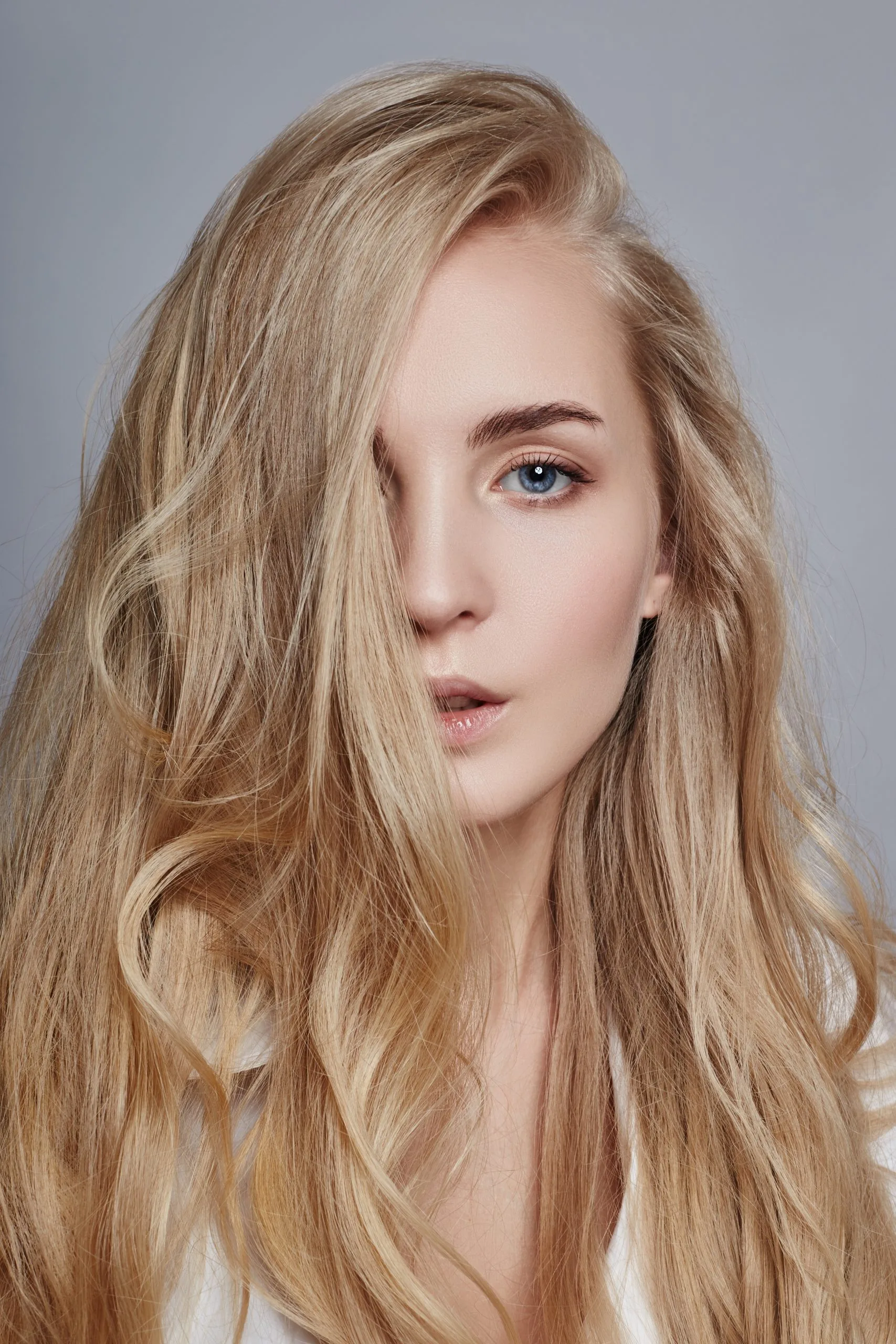 Woman with long blonde wavy hair in profile against gray background