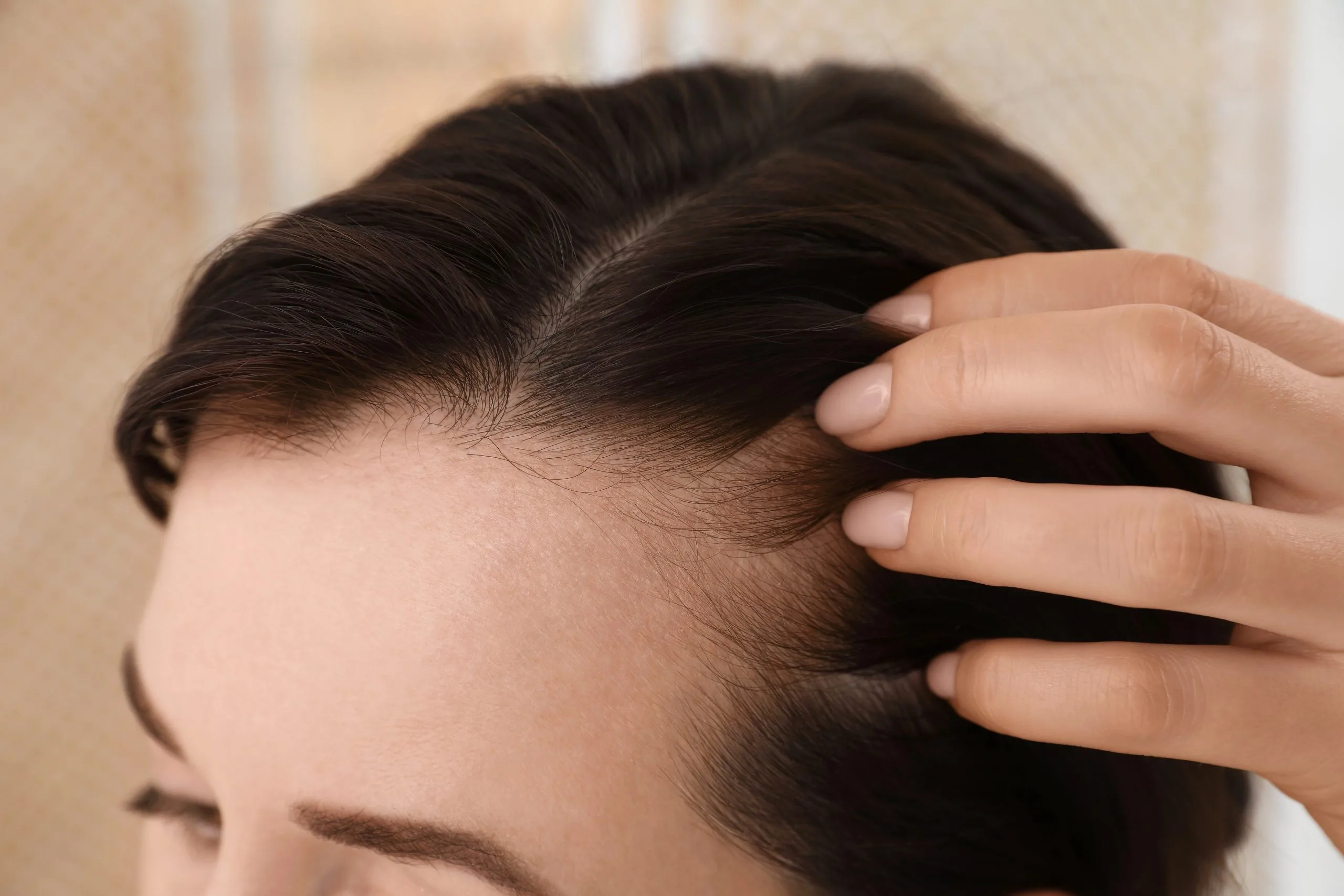 Woman showing thinning hair at her crown while examining scalp at home