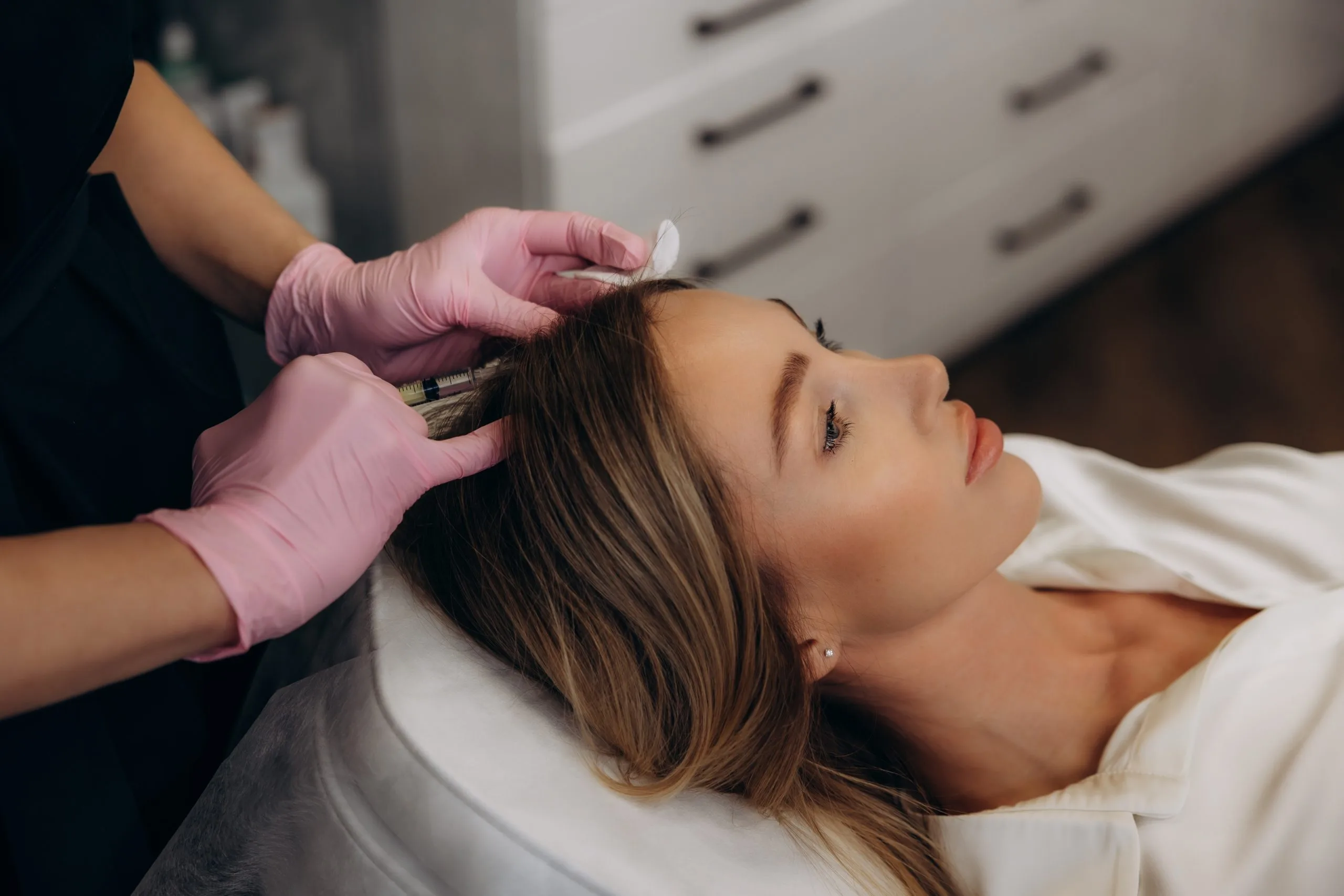 Gloved hands applying treatment to patient's forehead during facial procedure