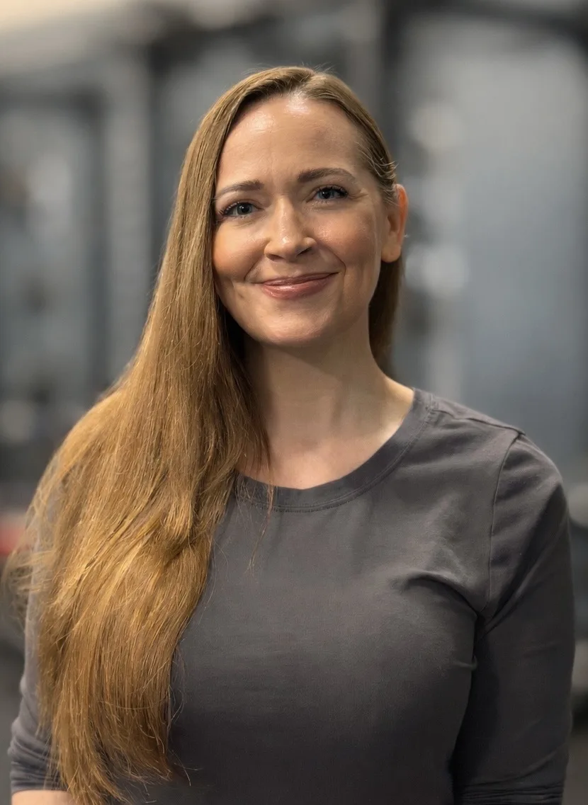 Anna Herron, LMT, portrait smiling at camera wearing grey shirt