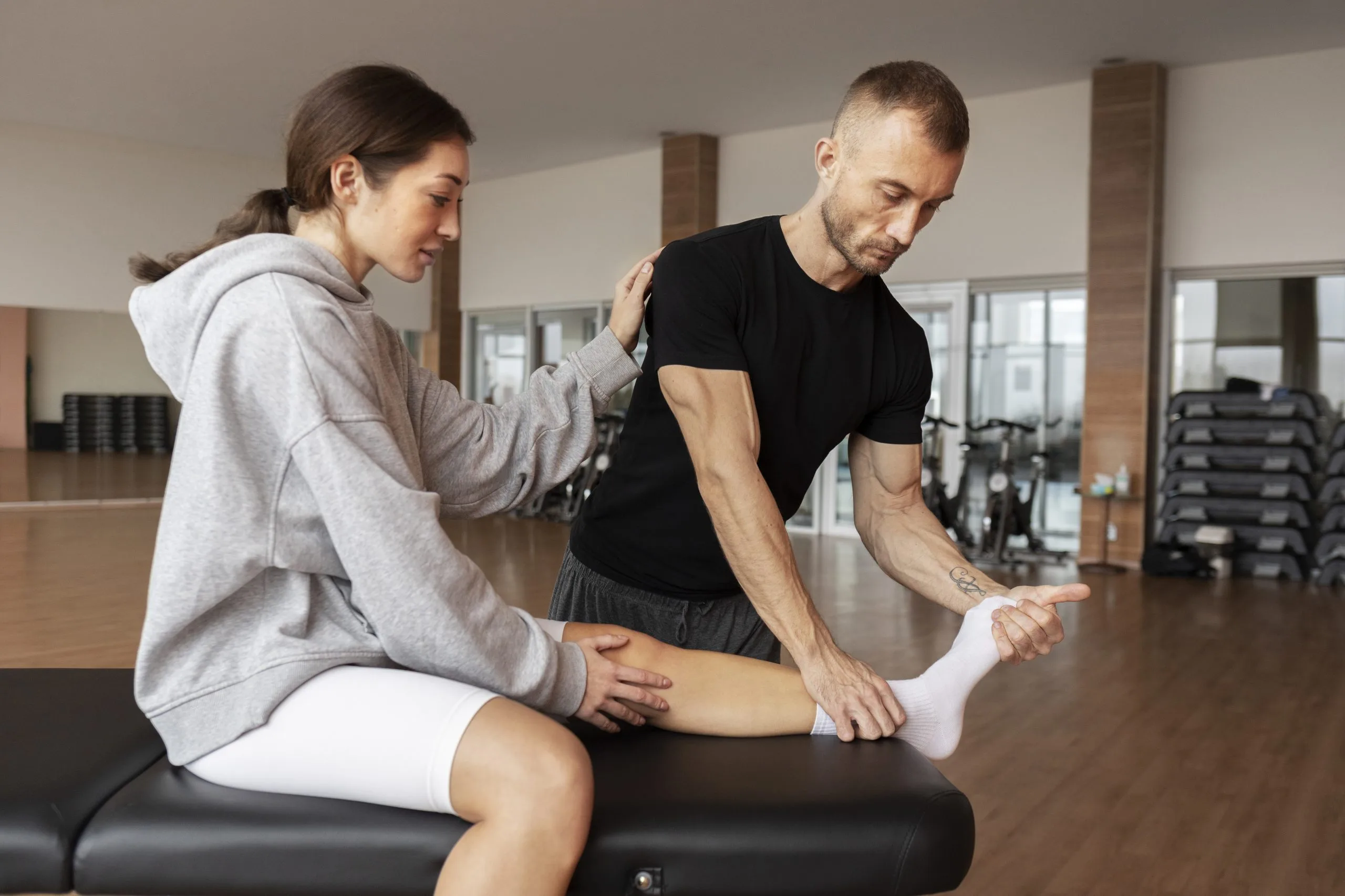Female physiotherapist assessing male patient's ankle mobility and flexibility in gym