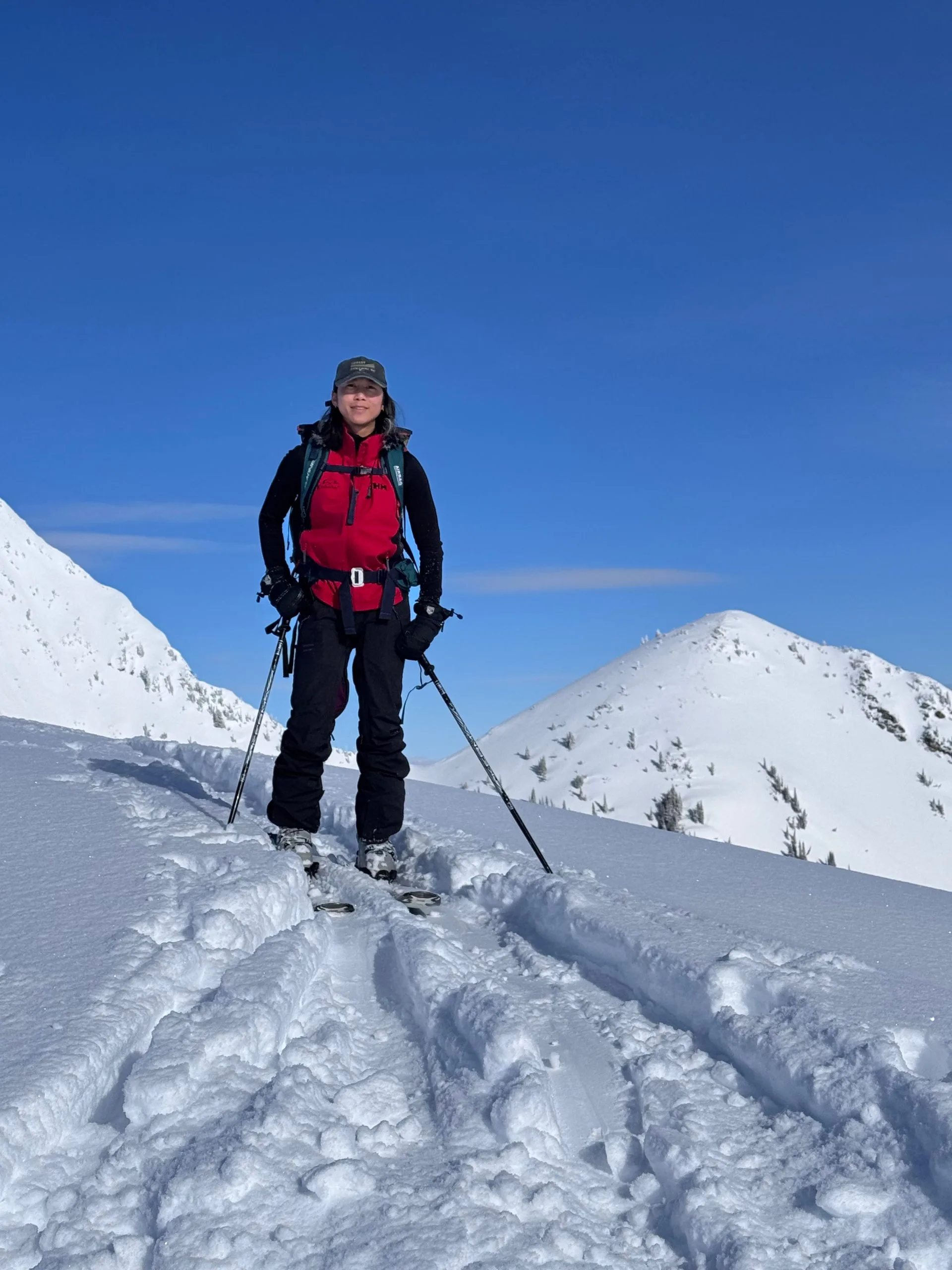 Woman skier in red jacket and cap on snowy slope with snow-covered mountains under clear blue sky