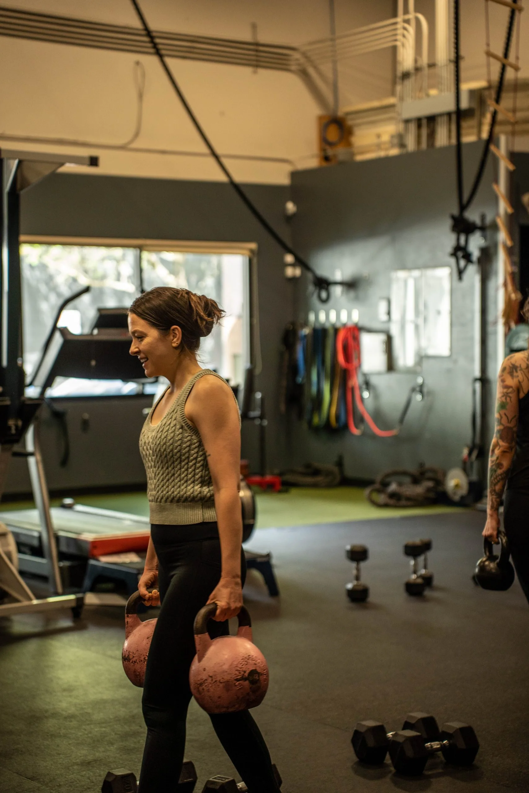 Woman holding kettlebells in a modern fitness studio with equipment and weights visible