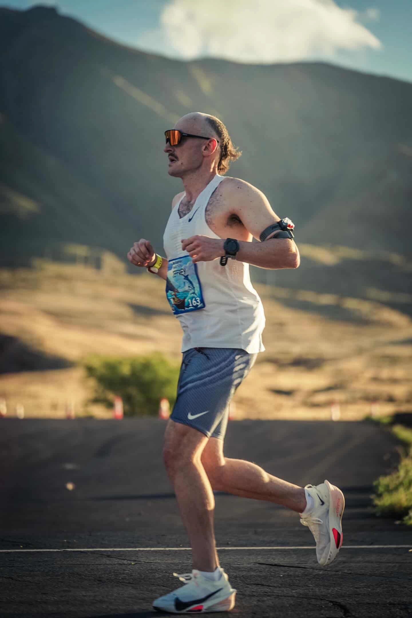 Jeffrey Leslie running on mountain road wearing race bib with sunglasses and smartwatch